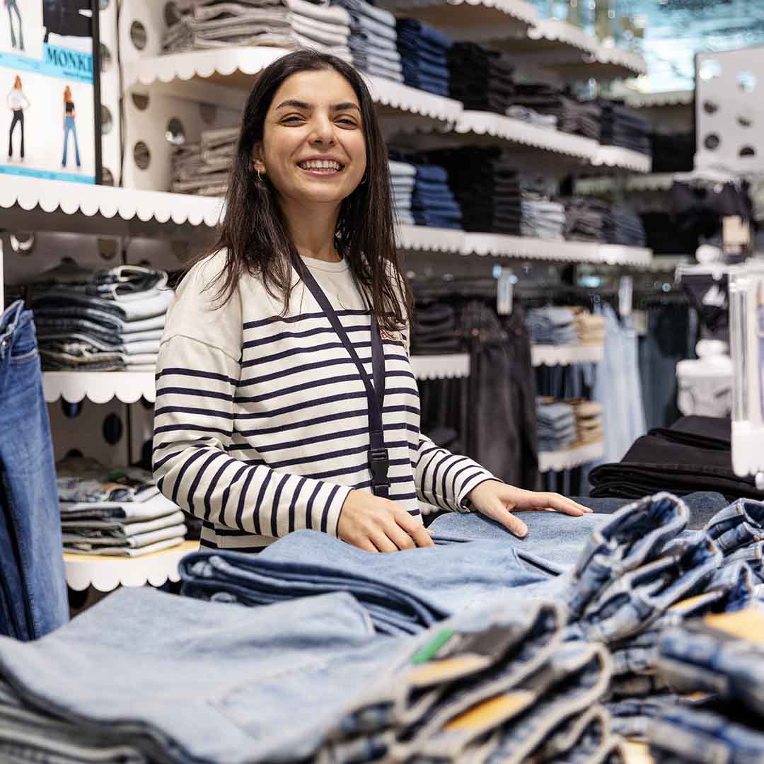 Smilende medarbejder fra Monki i Frederiksberg Centret, lægger jeans på hylder.